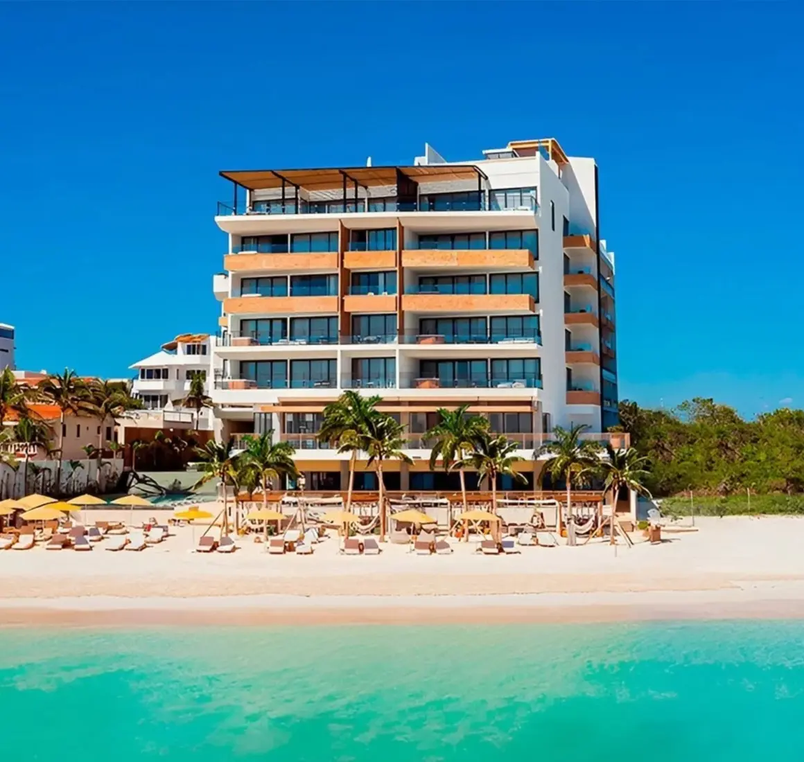 Beachfront resort with modern design, surrounded by palm trees and loungers, directly on a white sand shoreline.