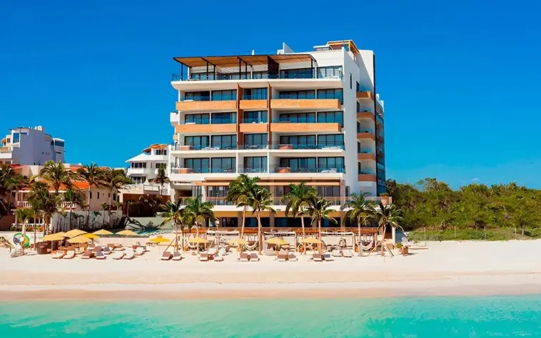 Beachfront resort with modern design, surrounded by palm trees and loungers, directly on a white sand shoreline.