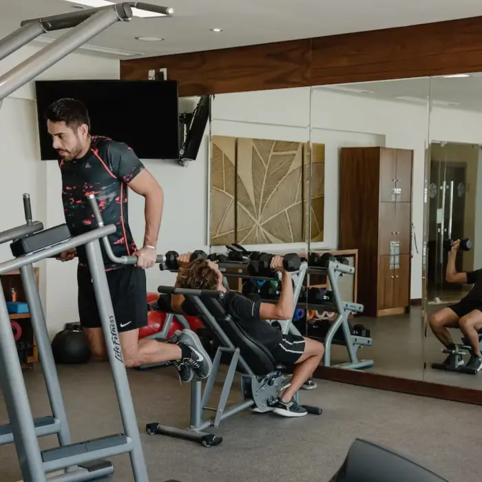 Guests exercising in the modern gym at The Reef 28, equipped with various fitness machines and mirrored walls.