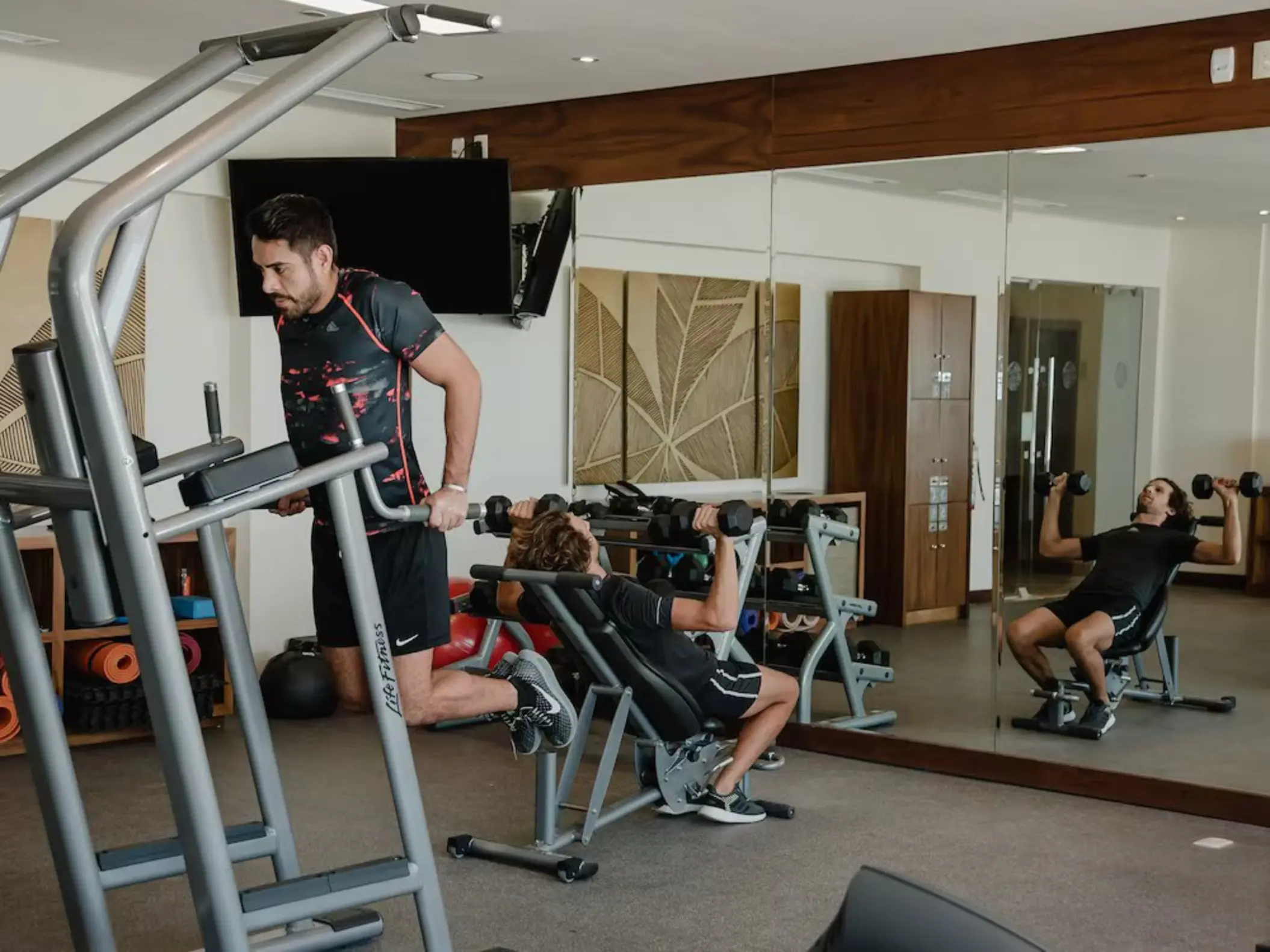 Guests exercising in the modern gym at The Reef 28, equipped with various fitness machines and mirrored walls.