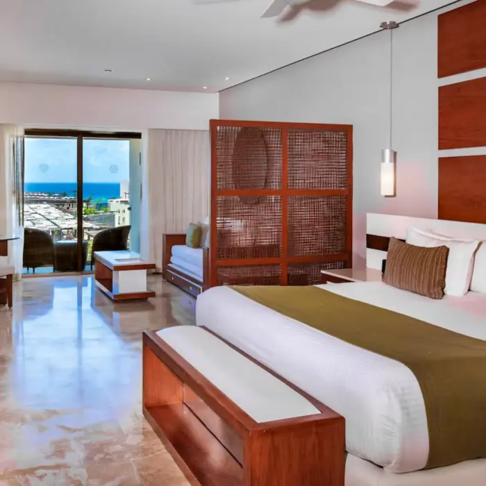 A well-appointed junior suite at The Reef 28 with a king-size bed and a balcony offering partial ocean views.