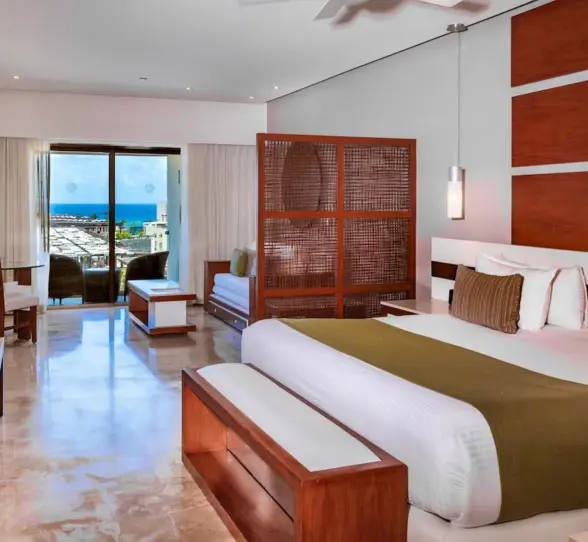 A well-appointed junior suite at The Reef 28 with a king-size bed and a balcony offering partial ocean views.