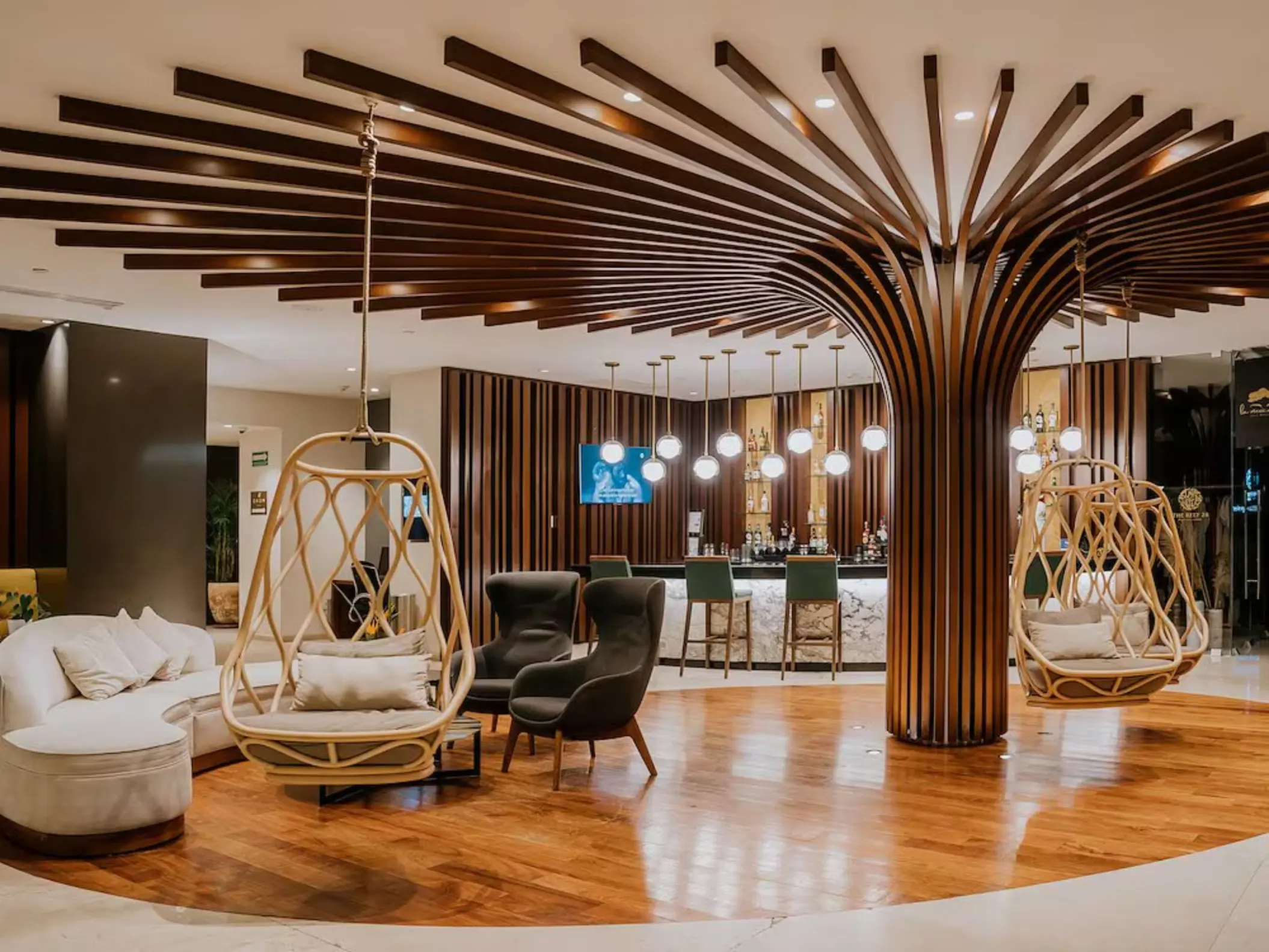 The stylish reception and lobby bar at The Reef 28, featuring unique tree-like wooden columns and hanging chairs.