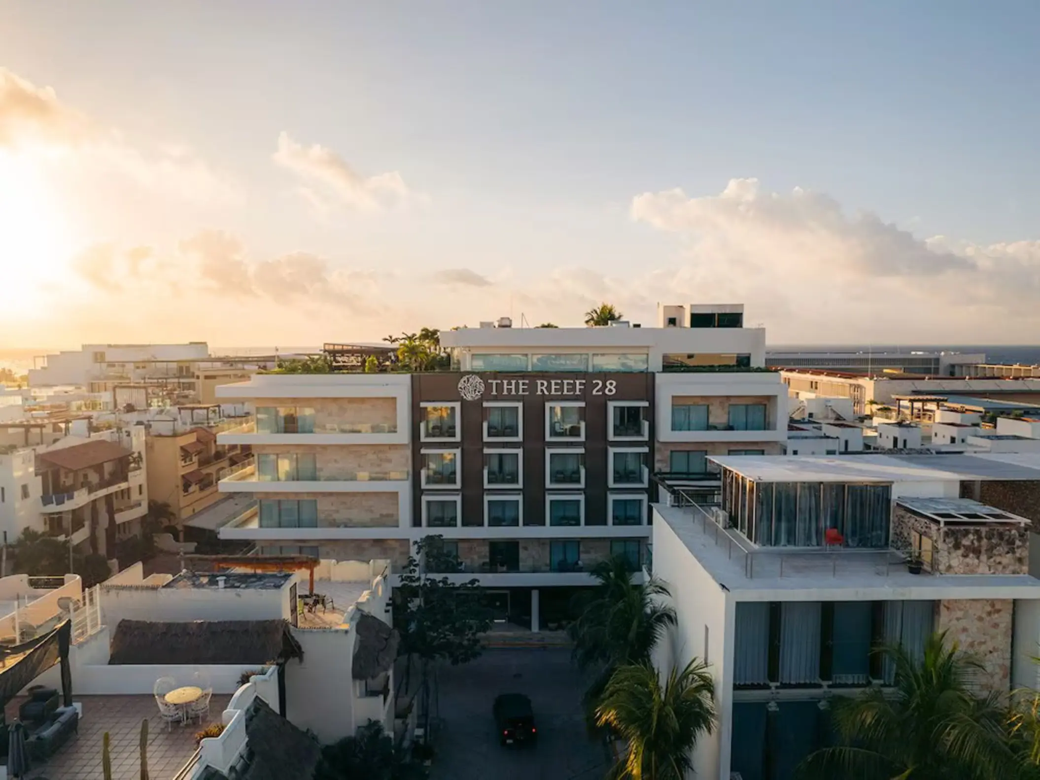 An aerial view of The Reef 28 hotel building and surrounding area during a beautiful sunset, with warm golden light.