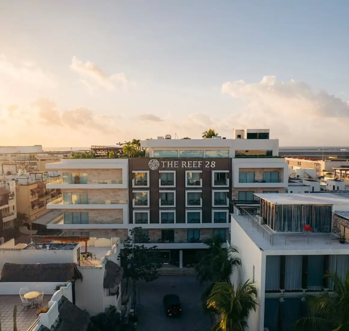 An aerial view of The Reef 28 hotel building and surrounding area during a beautiful sunset, with warm golden light.