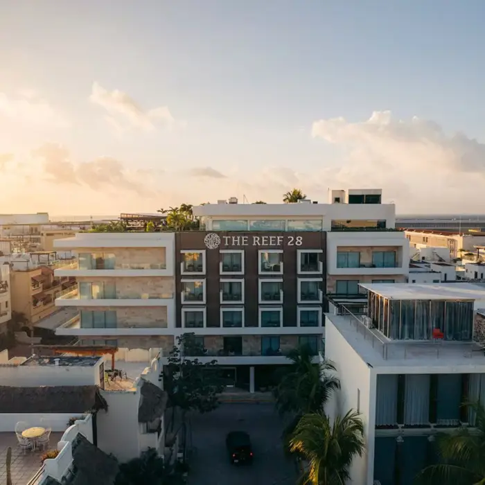 An aerial view of The Reef 28 hotel building and surrounding area during a beautiful sunset, with warm golden light.
