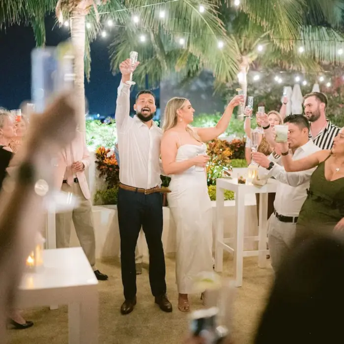 A joyful couple raising a toast at their outdoor wedding celebration at The Reef 28, surrounded by cheering guests at night.