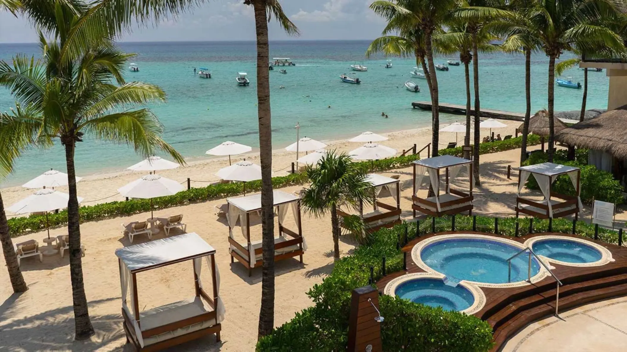 Aerial view of the hotel's hot tubs and beach with palm trees and sun umbrellas.