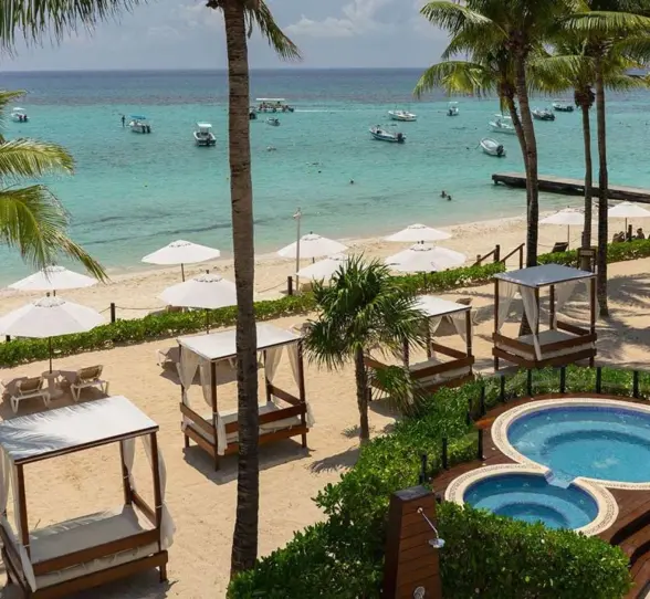 Aerial view of the hotel's hot tubs and beach with palm trees and sun umbrellas.