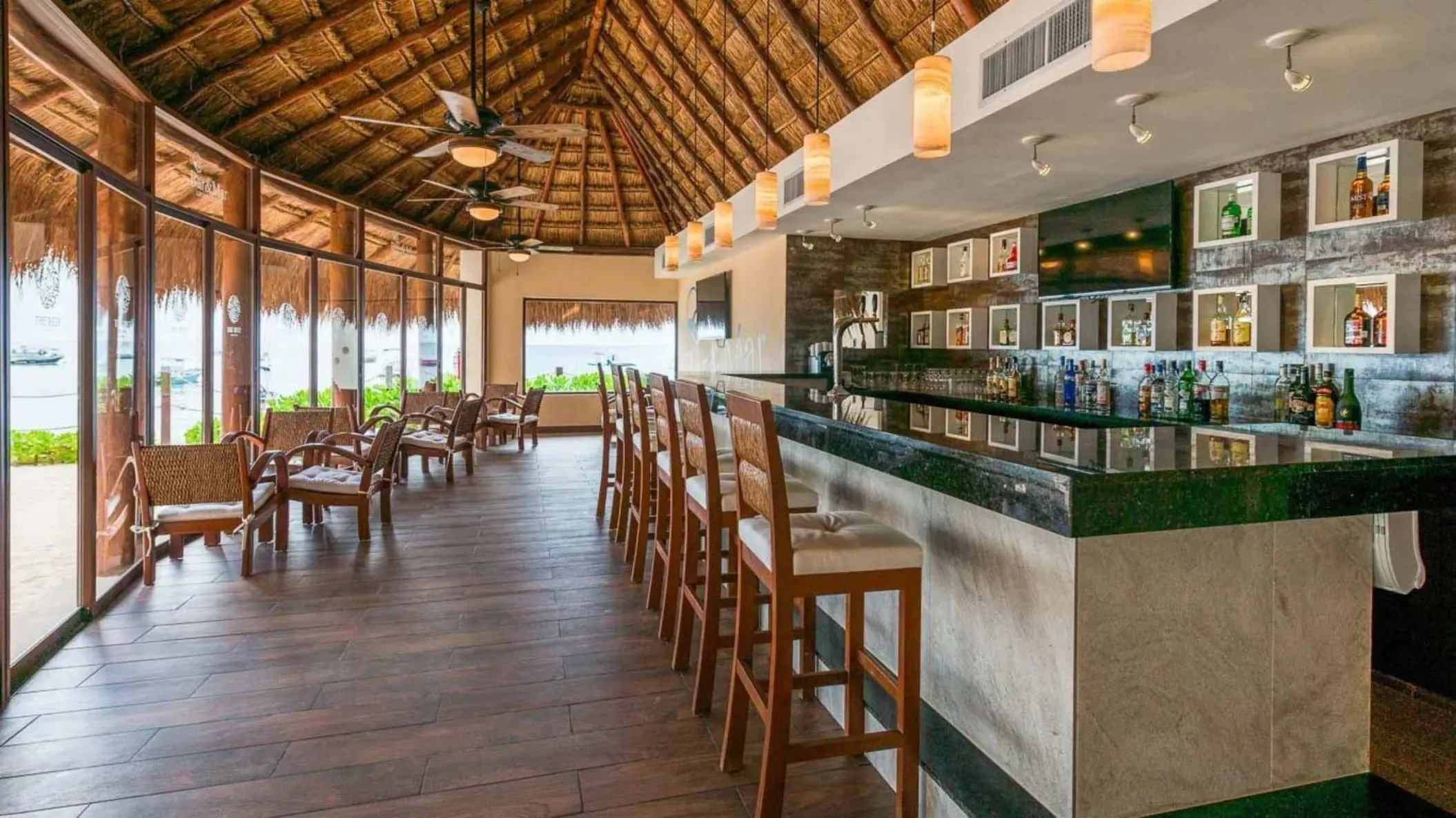 Interior shot of the hotel's thatched-roof bar with wooden chairs and a fully stocked counter.