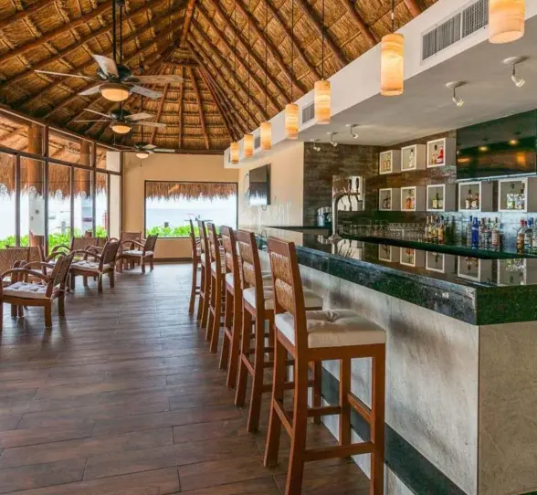 Interior shot of the hotel's thatched-roof bar with wooden chairs and a fully stocked counter.