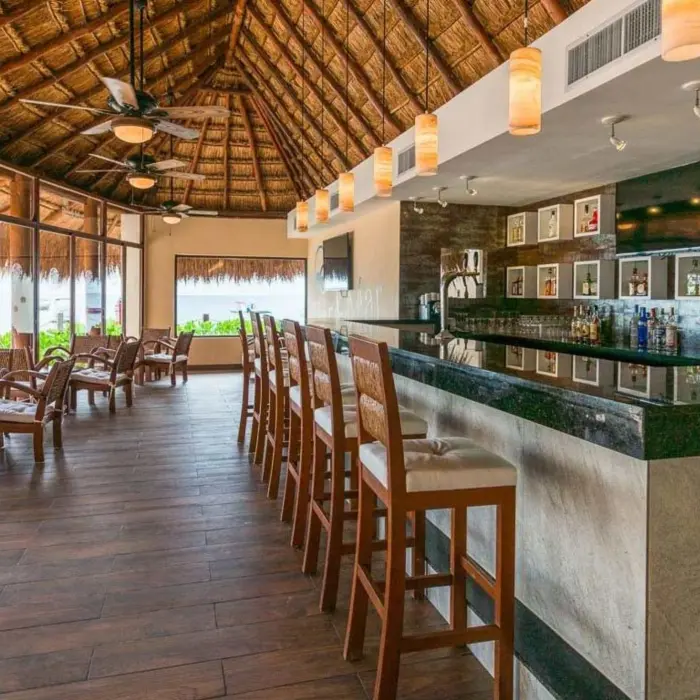 Interior shot of the hotel's thatched-roof bar with wooden chairs and a fully stocked counter.