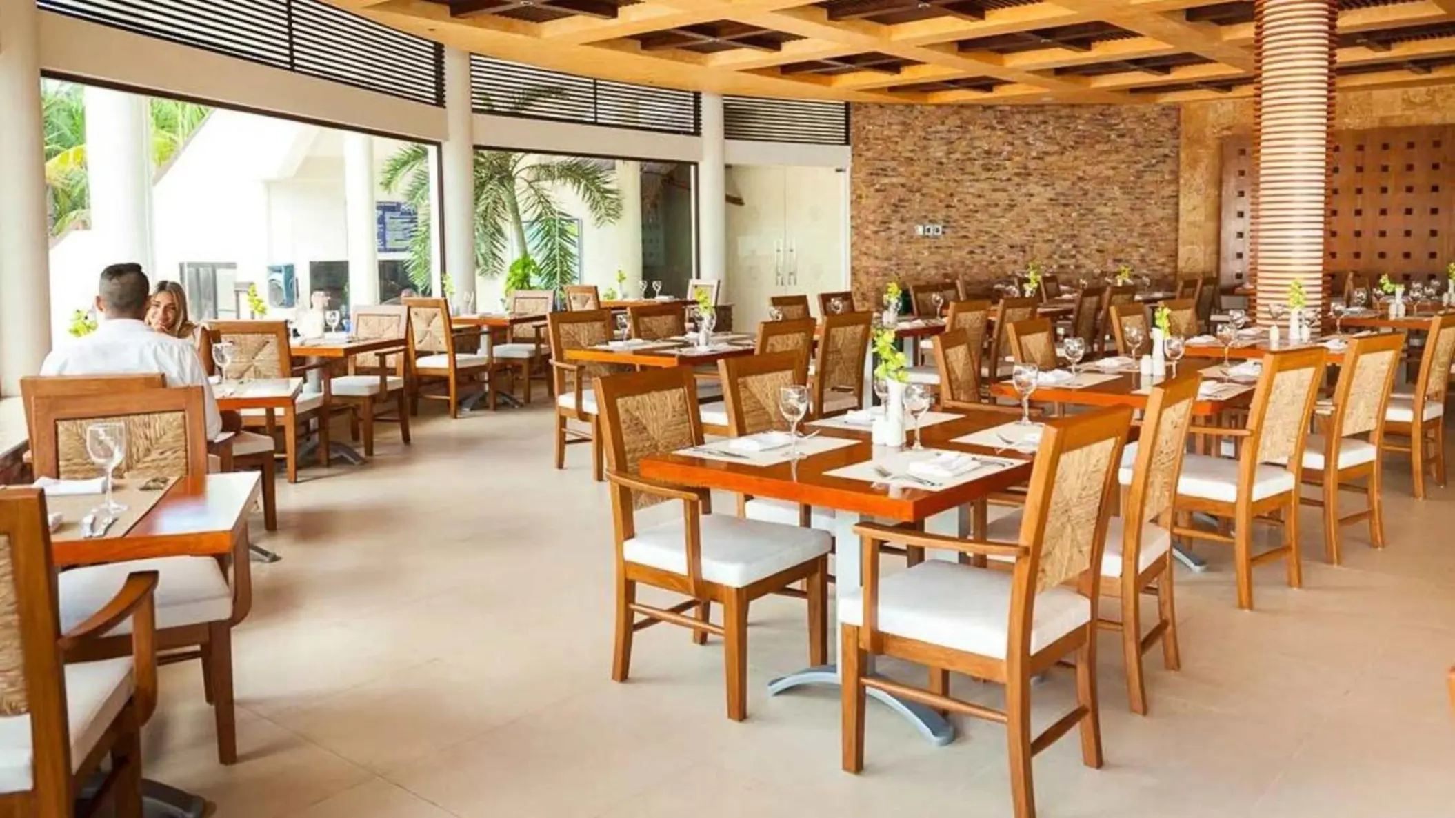 A couple dining at a restaurant with modern wooden tables, chairs, and large windows.