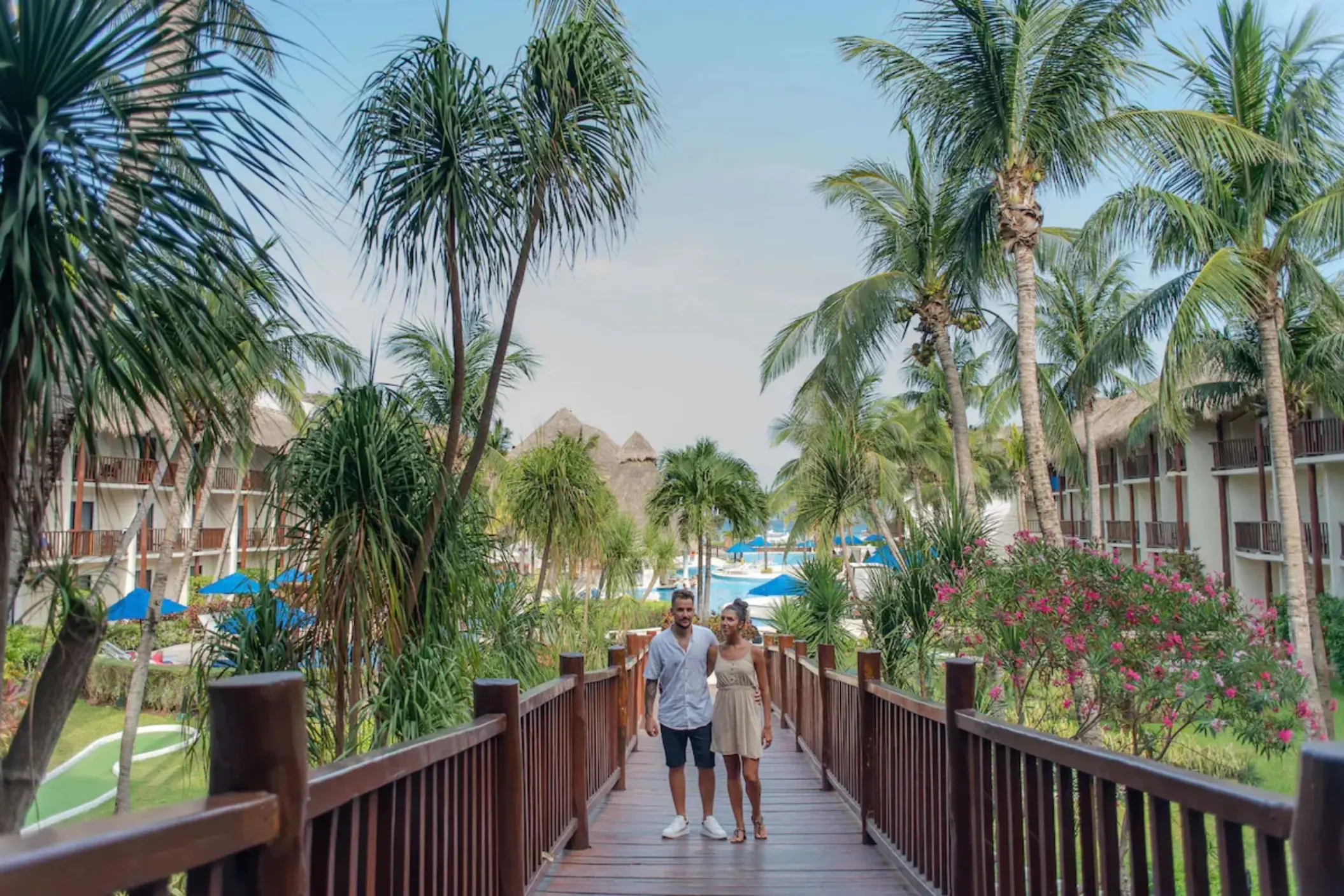 A couple walking on a wooden bridge through a lush tropical garden with palm trees.