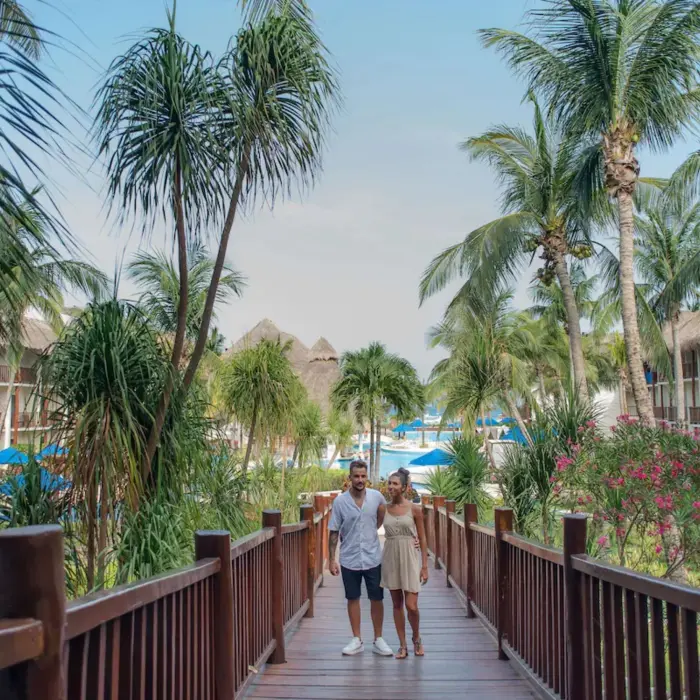 A couple walking on a wooden bridge through a lush tropical garden with palm trees.