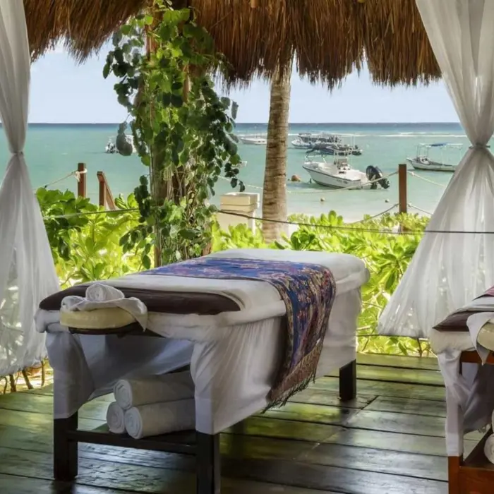 Two massage beds under a thatched roof with white curtains and a view of the sea.