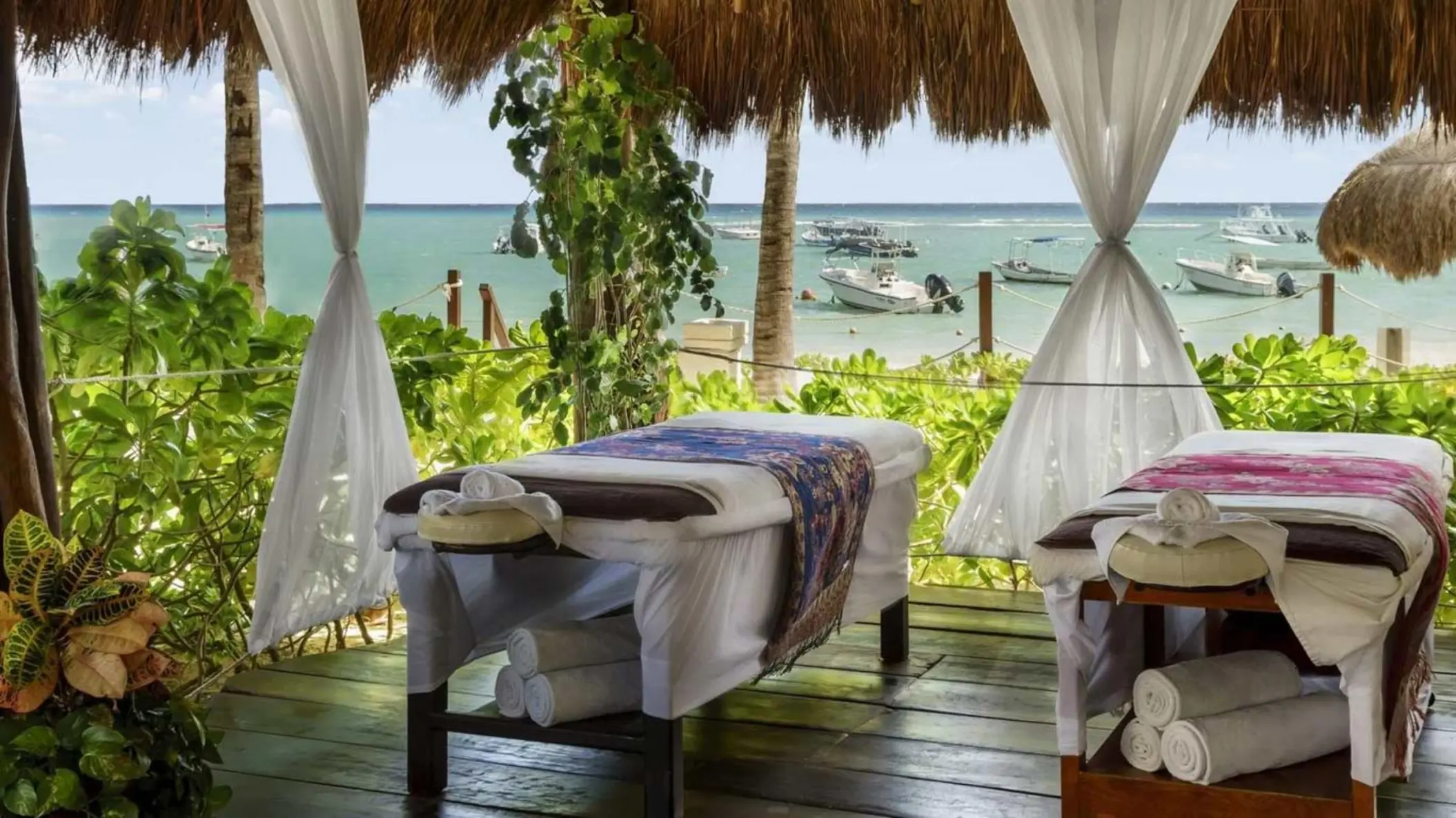 Two massage beds under a thatched roof with white curtains and a view of the sea.
