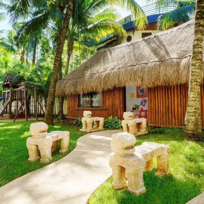 A children's playground with a slide and a small thatched-roof hut surrounded by palm trees.