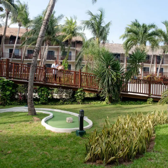 A mini-golf course surrounded by lush green lawn and palm trees with a couple in the background.
