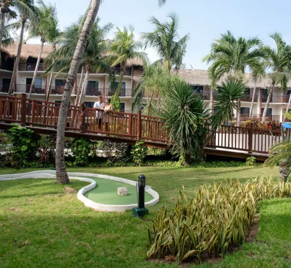 A mini-golf course surrounded by lush green lawn and palm trees with a couple in the background.