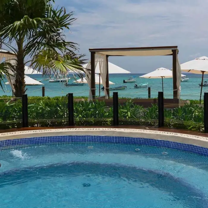 An oceanfront hot tub with a view of the beach, palm trees, and ocean.