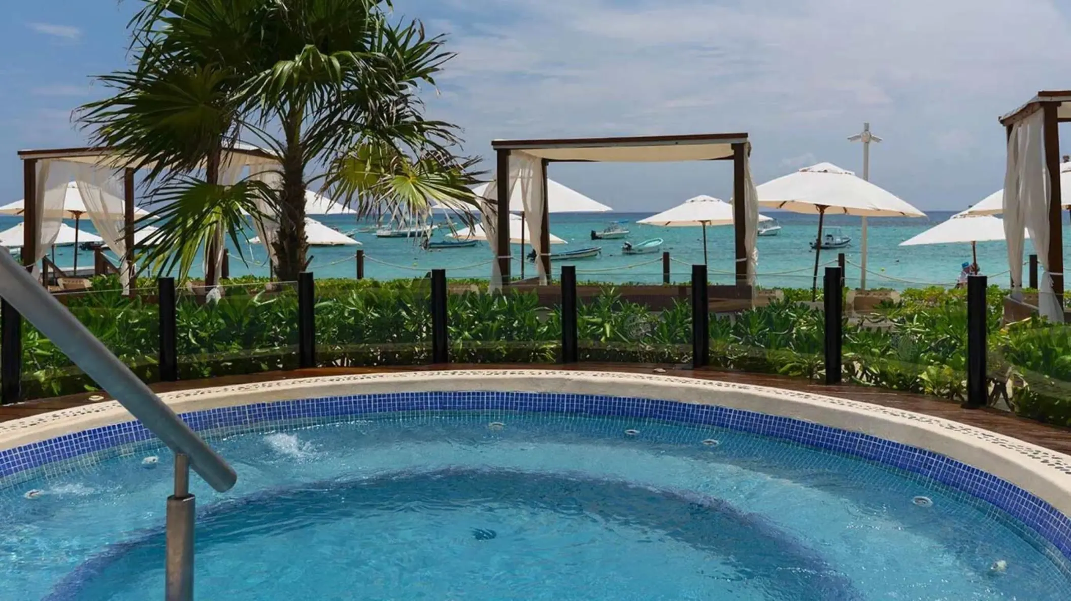 An oceanfront hot tub with a view of the beach, palm trees, and ocean.