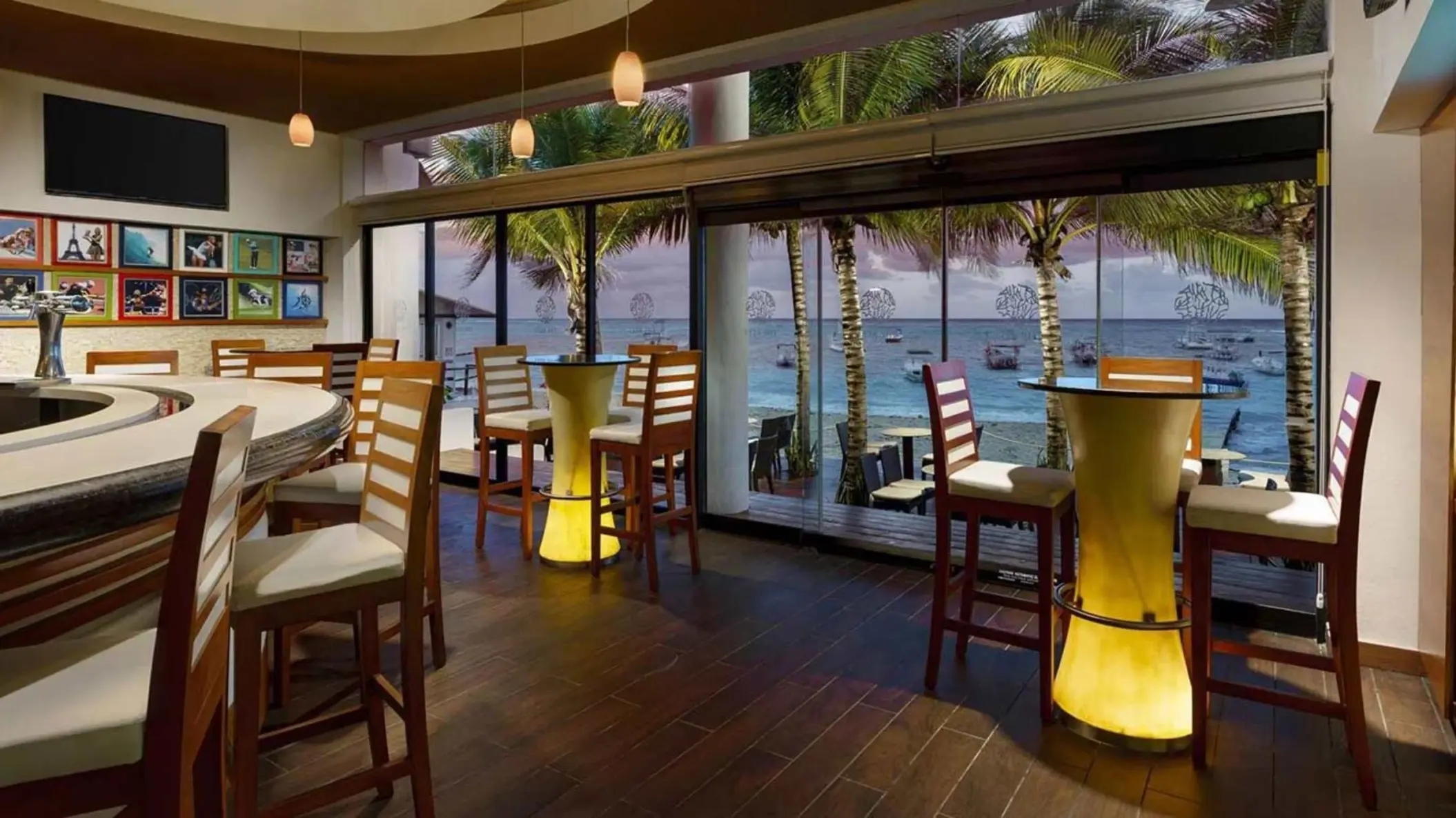 An oceanfront restaurant with a bar, high-top tables, and a view of the beach and ocean.