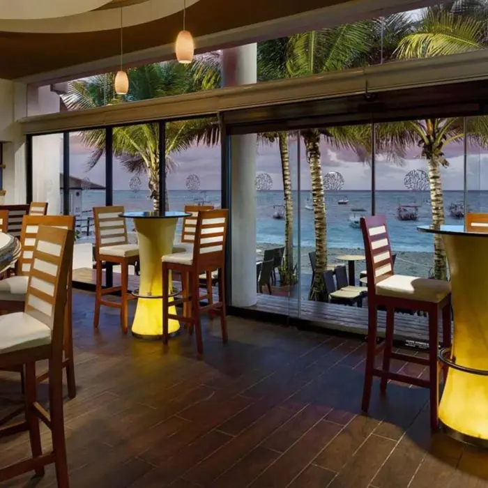 An oceanfront restaurant with a bar, high-top tables, and a view of the beach and ocean.