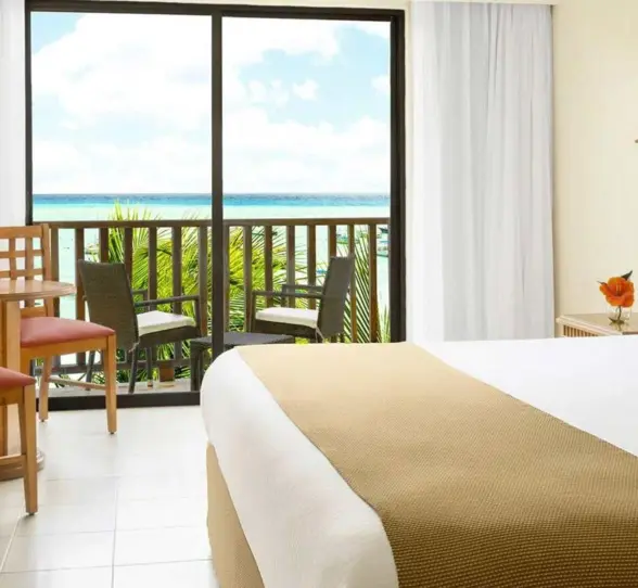 A bright hotel room with a bed and a balcony overlooking the sea.