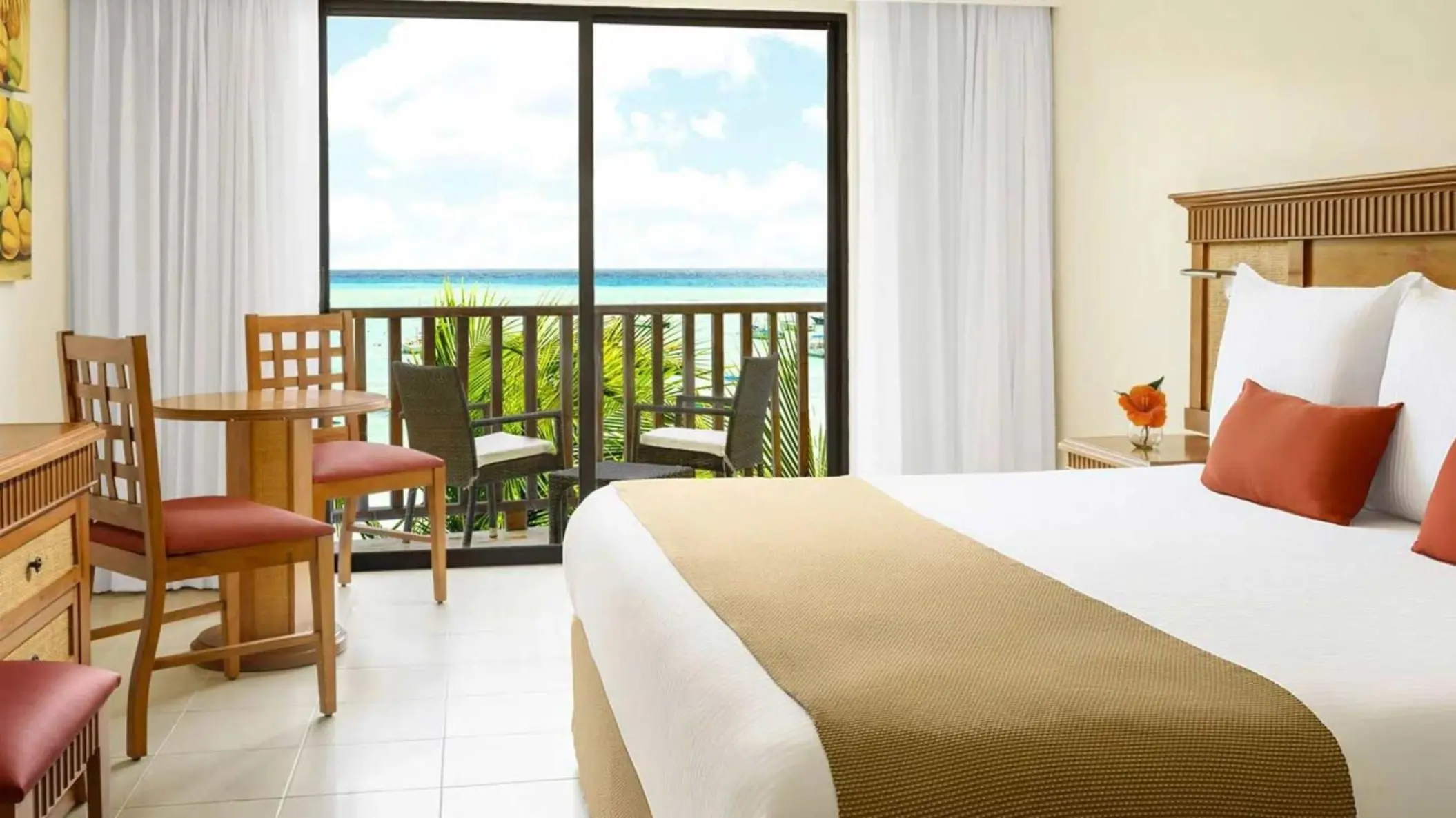 A bright hotel room with a bed and a balcony overlooking the sea.
