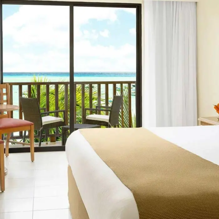A bright hotel room with a bed and a balcony overlooking the sea.