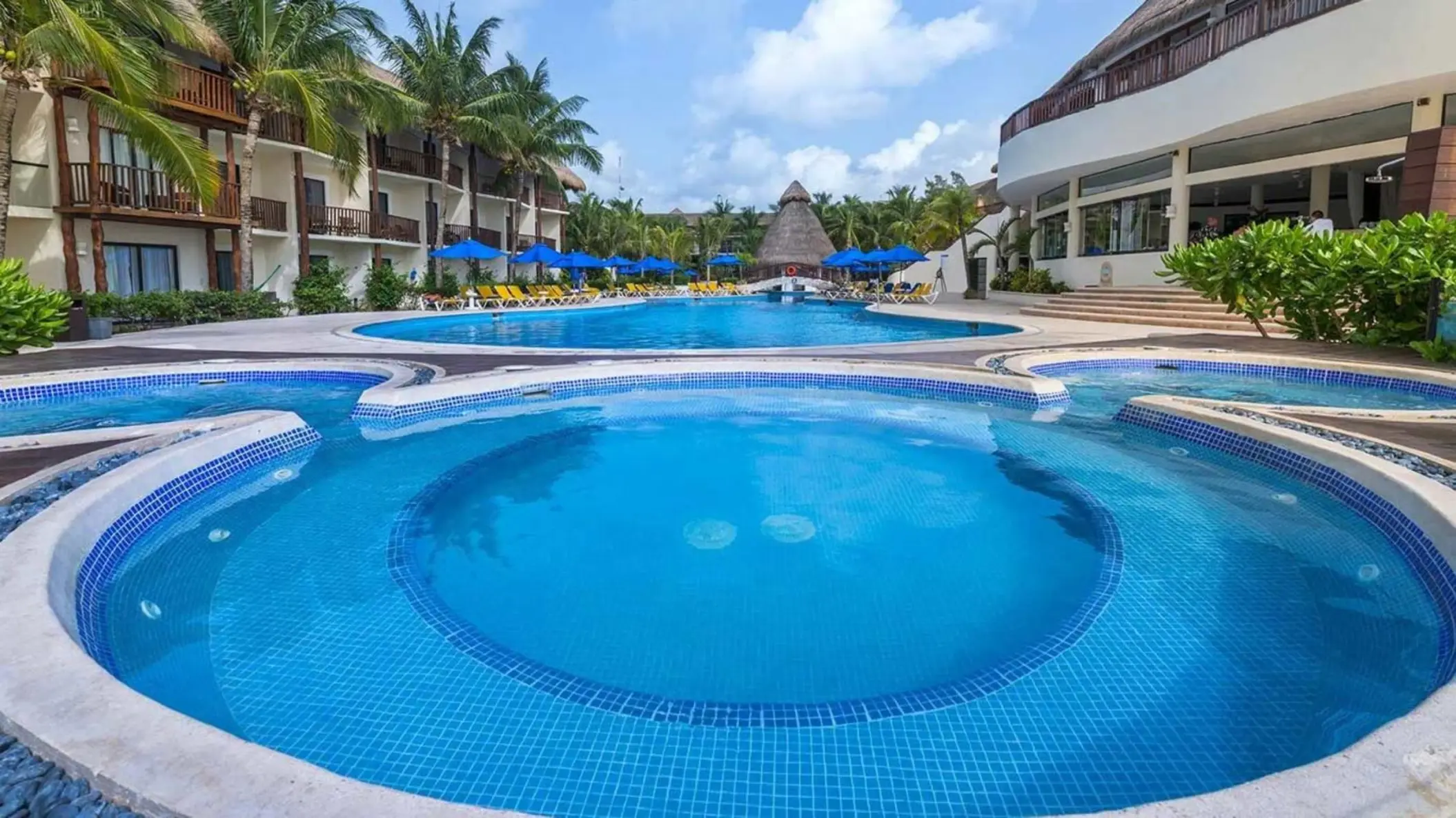 A large, multi-level swimming pool area surrounded by lounge chairs and palm trees.