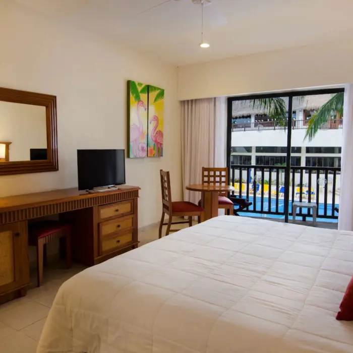 A hotel room with a large bed and a balcony offering a view of the swimming pool.