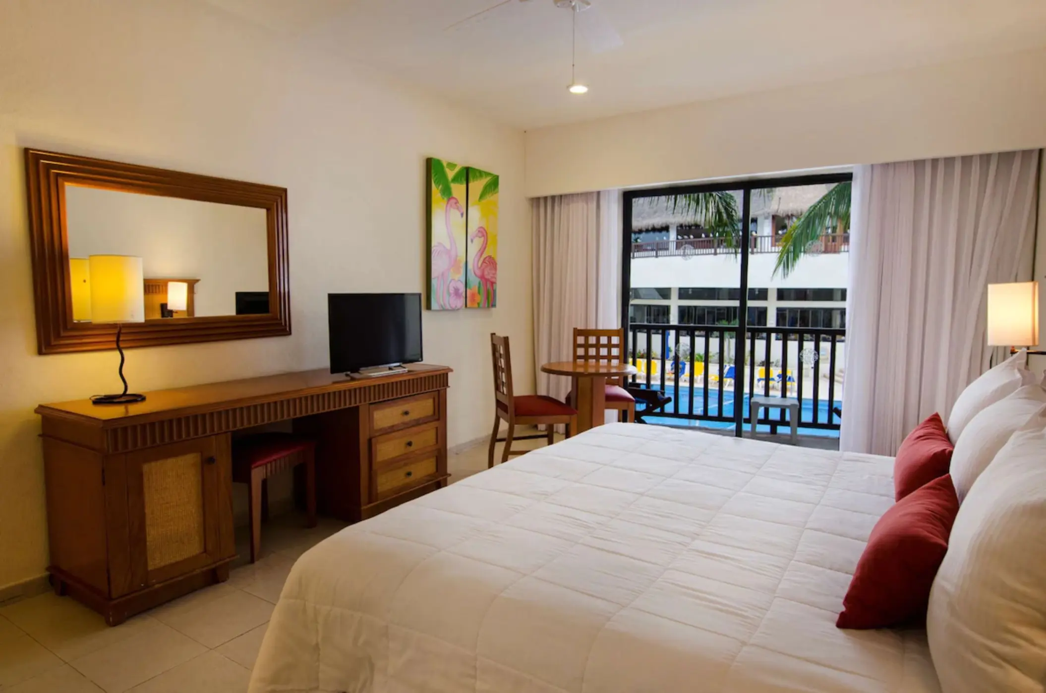 A hotel room with a large bed and a balcony offering a view of the swimming pool.