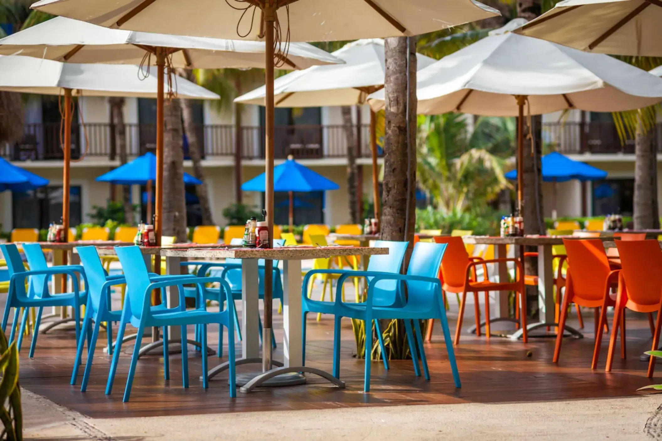 An outdoor snack bar area with colorful tables, chairs, and large umbrellas.
