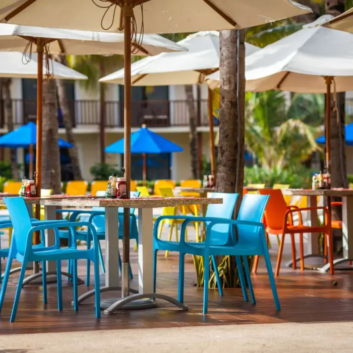An outdoor snack bar area with colorful tables, chairs, and large umbrellas.