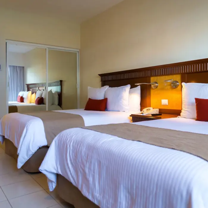 A hotel suite with two beds, a tiled floor, and a mirror-doored closet.