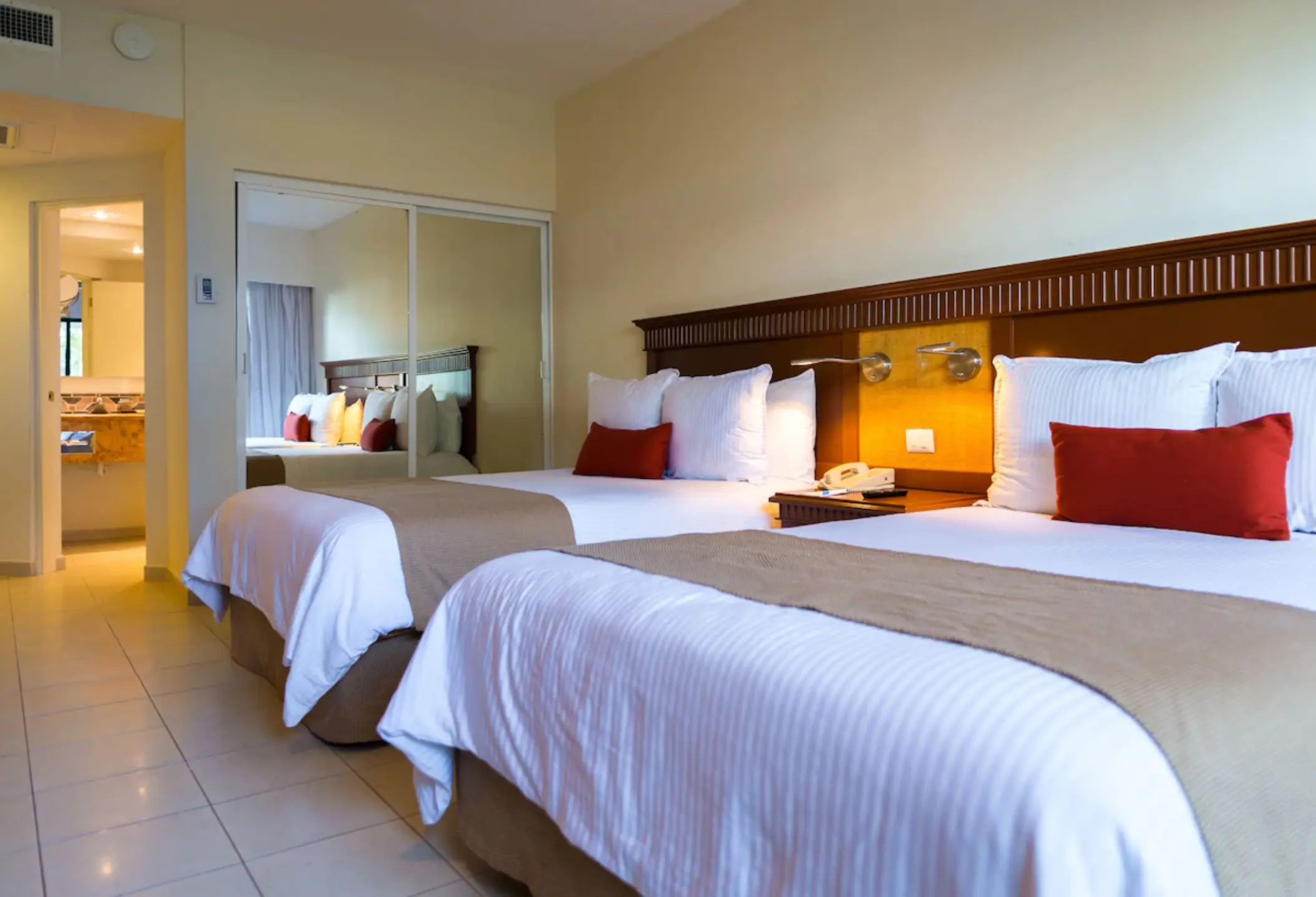 A hotel suite with two beds, a tiled floor, and a mirror-doored closet.