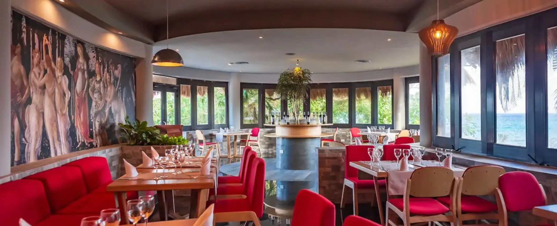 The interior of Botticelli restaurant at The Reef Playacar, featuring red seating, elegant table settings, and a large mural.