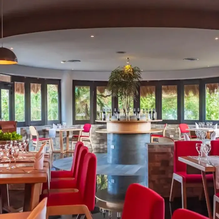 The interior of Botticelli restaurant at The Reef Playacar, featuring red seating, elegant table settings, and a large mural.