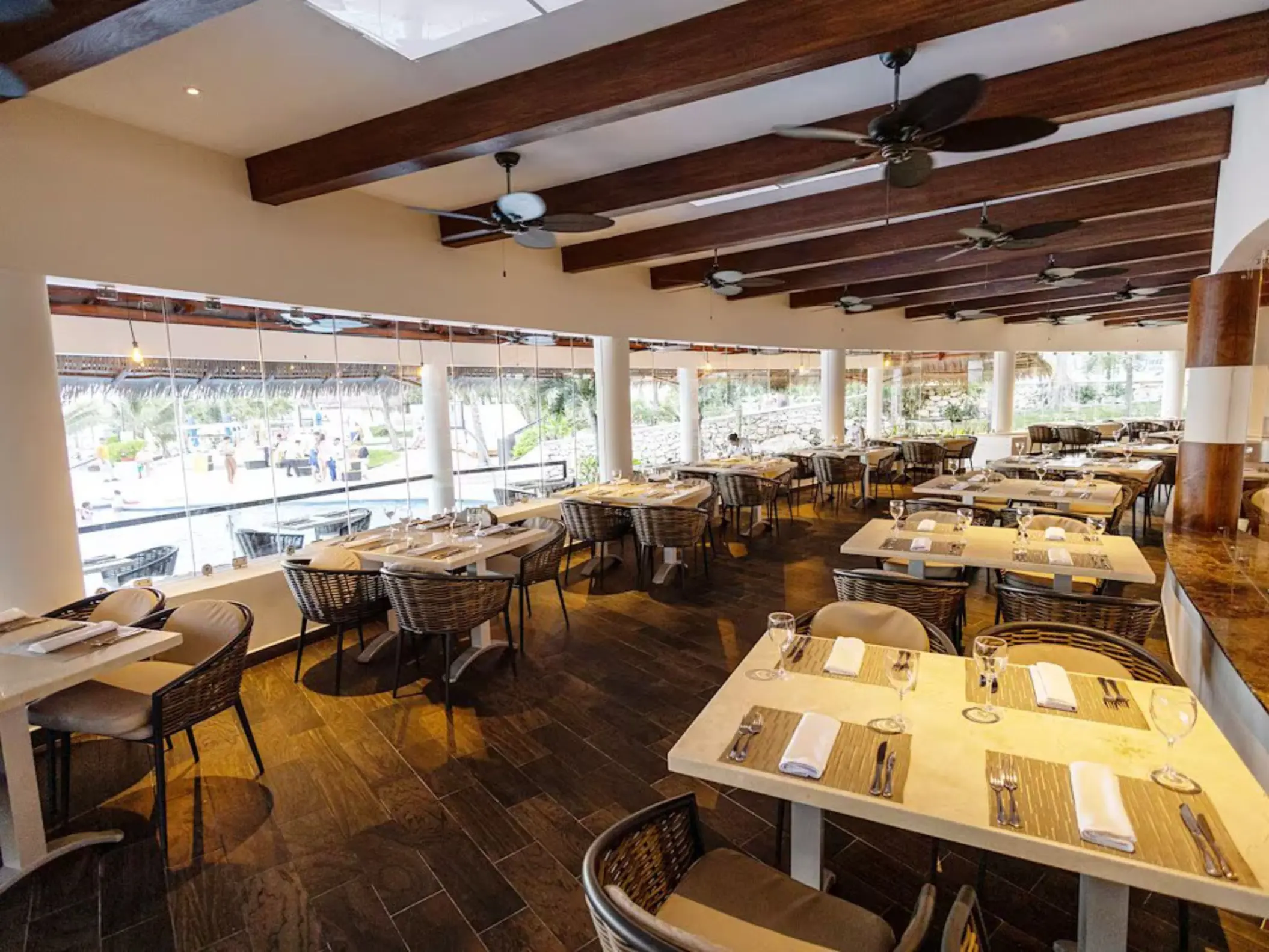 Interior of the spacious Chulavista restaurant at The Reef Playacar, featuring many dining tables and large windows overlooking a pool area.