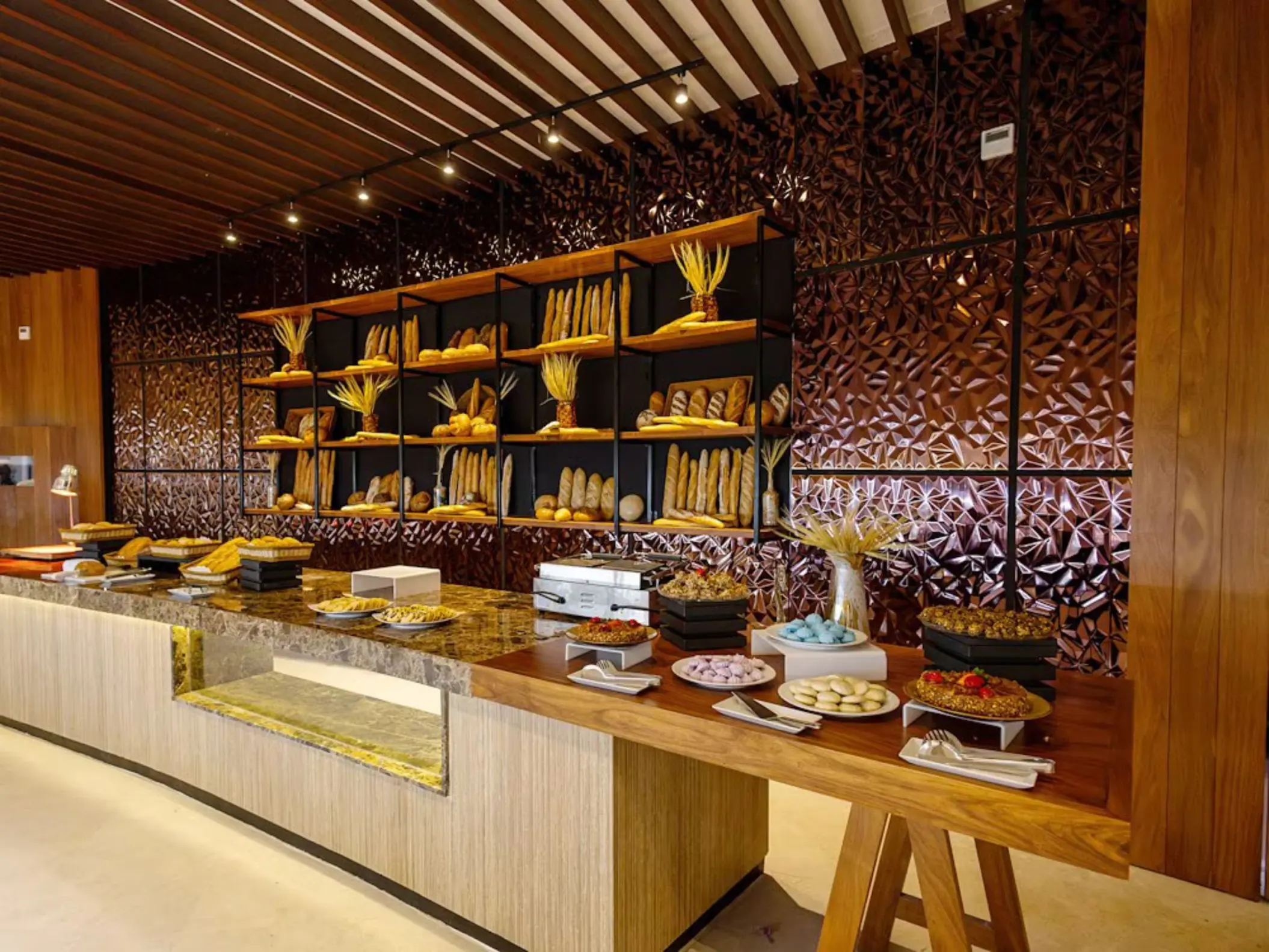 A buffet display of various desserts and baked goods on a long counter in a restaurant at The Reef Playacar.