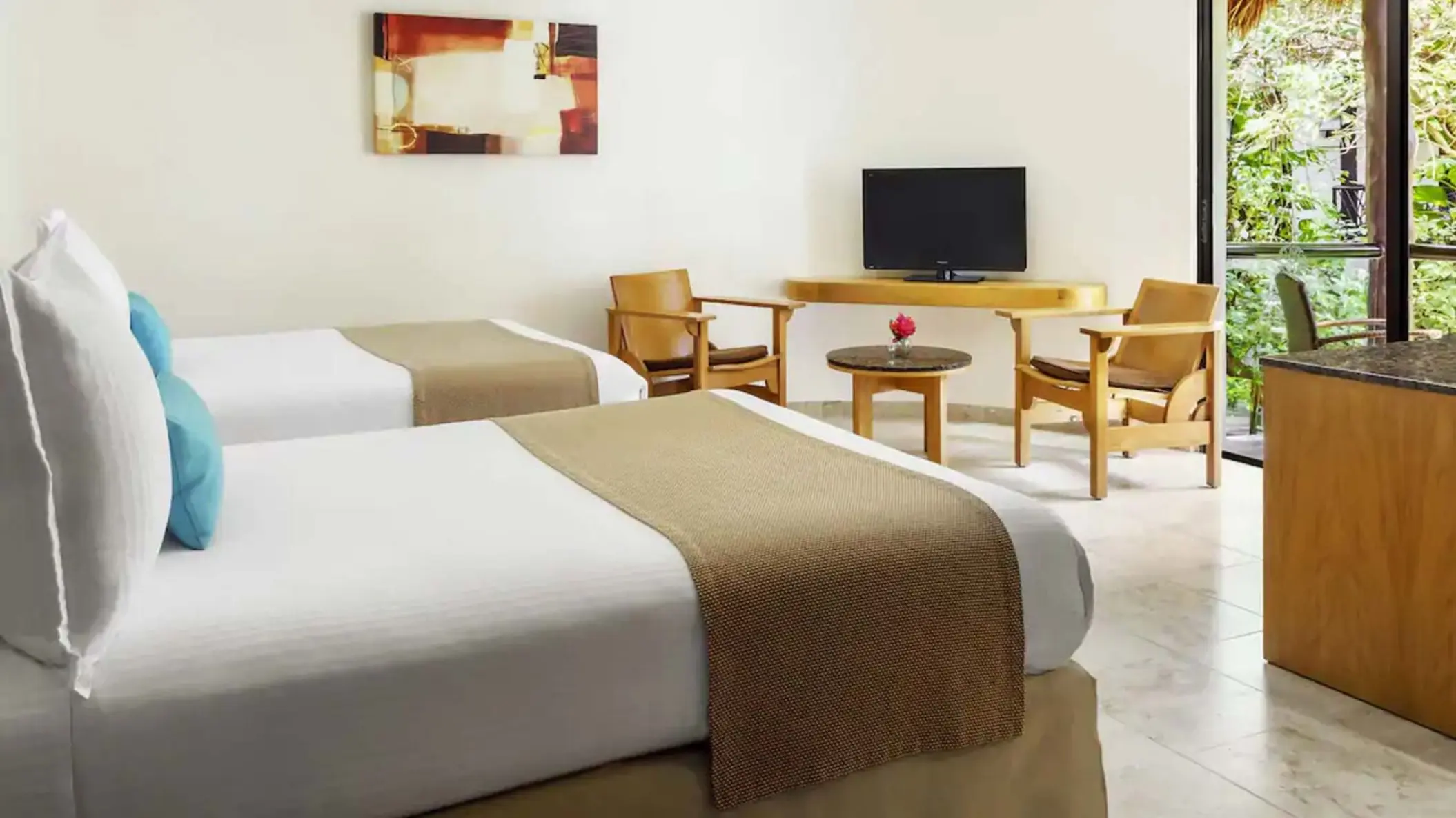 A comfortable suite at The Reef Playacar featuring two beds with beige throws, a flat-screen TV, and wooden chairs.