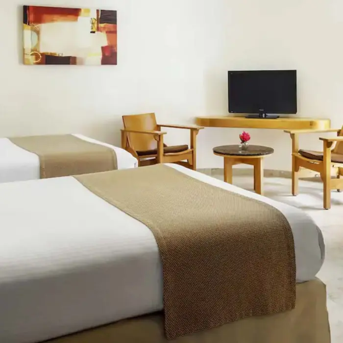 A comfortable suite at The Reef Playacar featuring two beds with beige throws, a flat-screen TV, and wooden chairs.