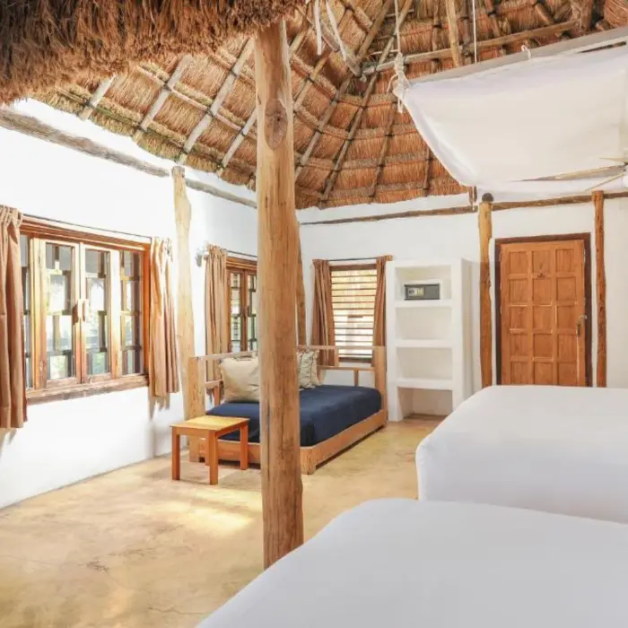 A hotel room with two beds, a thatched roof, white walls, and tropical views.