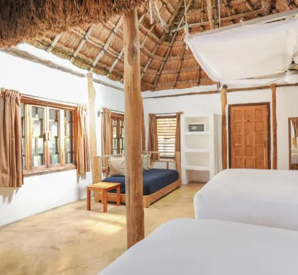 A hotel room with two beds, a thatched roof, white walls, and tropical views.