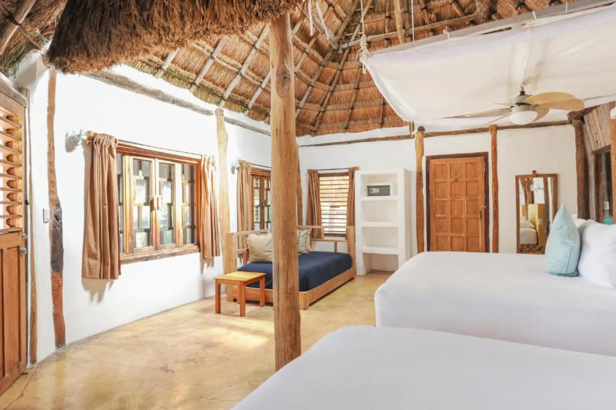 A hotel room with two beds, a thatched roof, white walls, and tropical views.