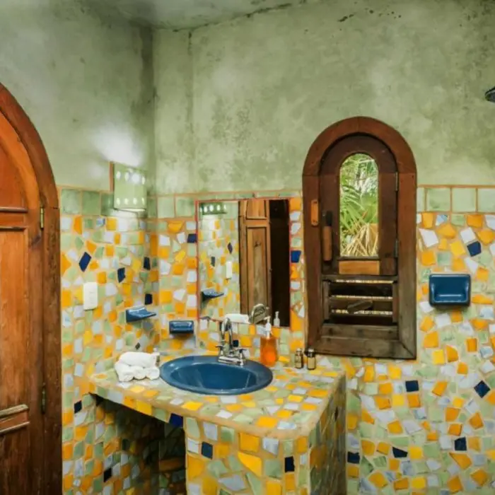 A vibrant rustic washroom with bright mosaic tiles on the walls and a large, arched wooden door.