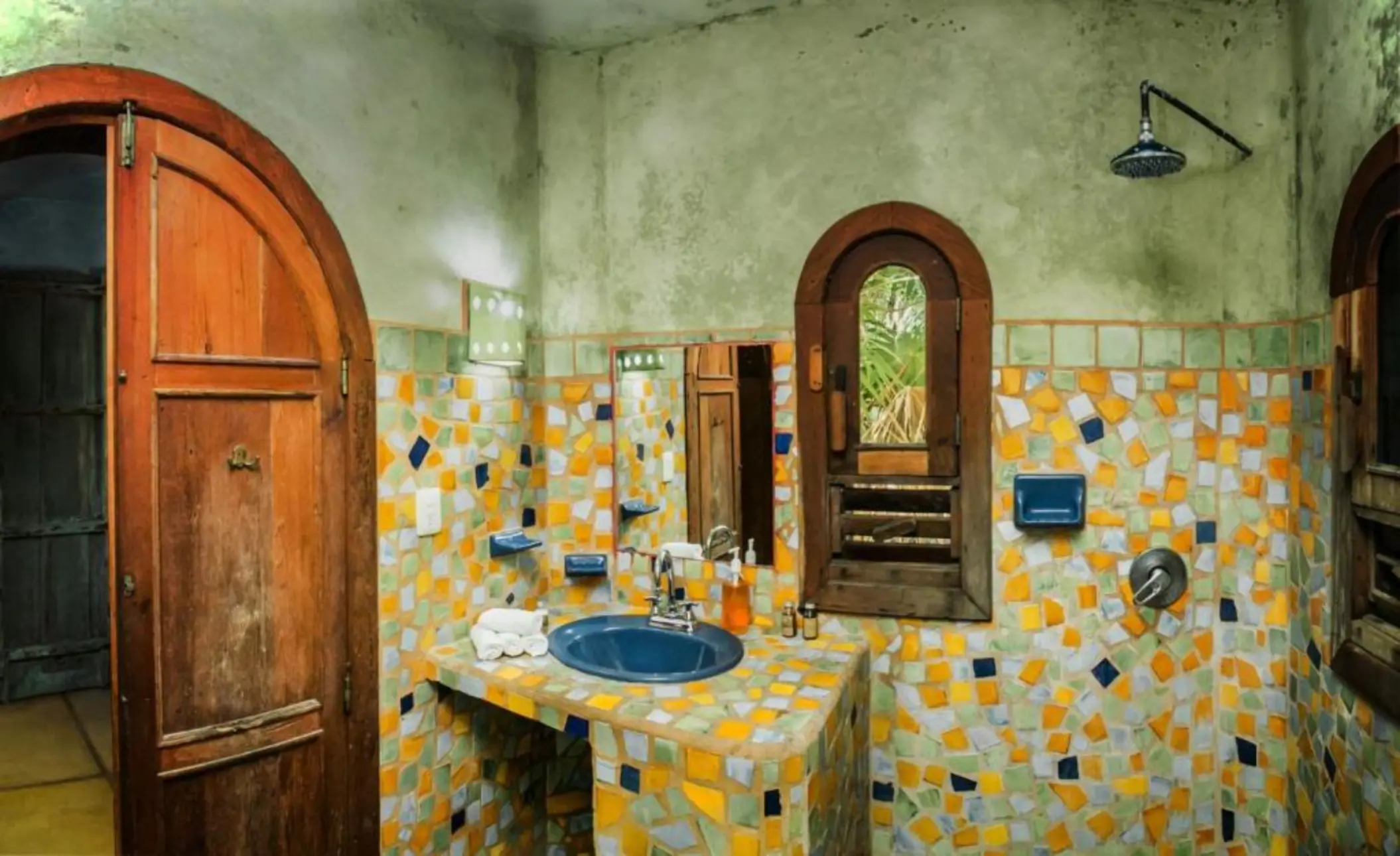 A vibrant rustic washroom with bright mosaic tiles on the walls and a large, arched wooden door.