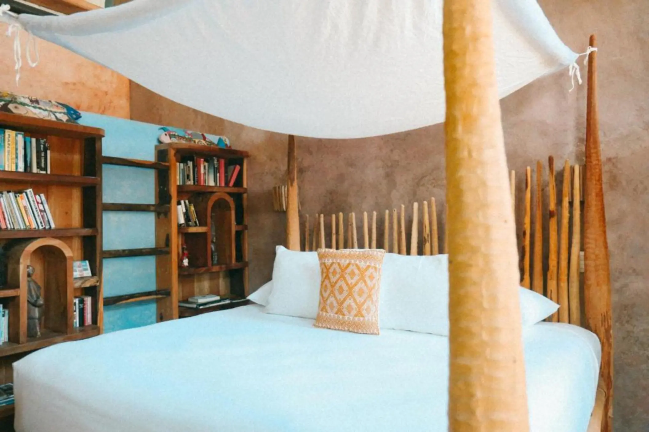 A rustic villa bedroom with wooden bookshelves, a canopy bed, and a decorative orange pillow.